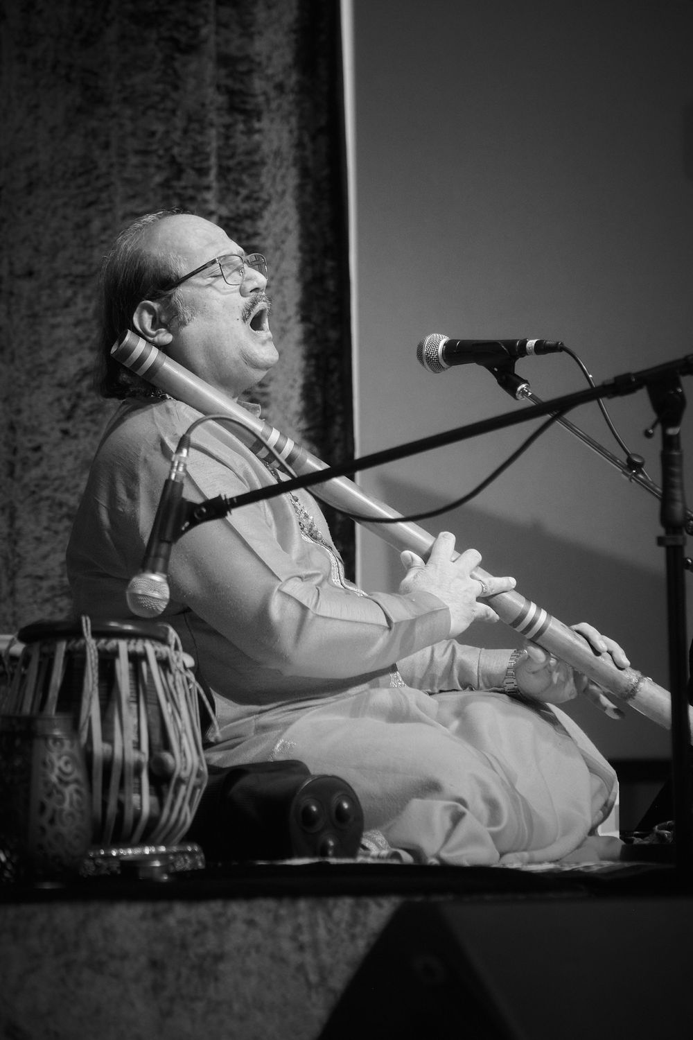 Classical musician performs passionately while sitting on stage in traditional attire during a concert performance.