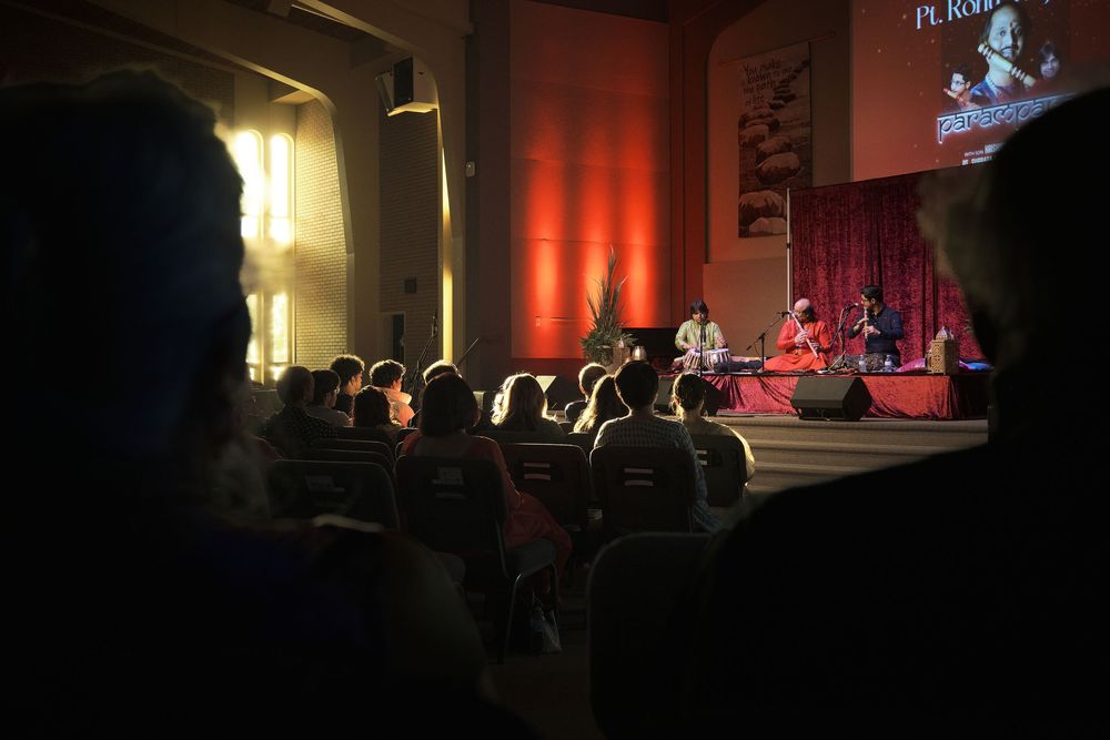 Dark concert hall with dramatic red and yellow lighting illuminating the stage and silhouetted audience members.