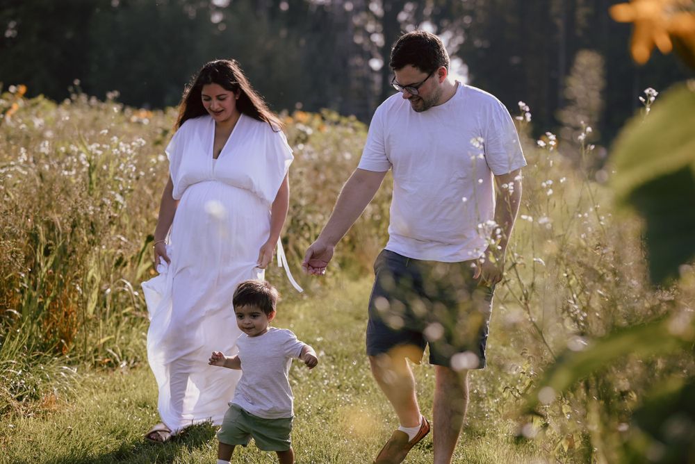 Family spending quality time together while walking through a sunlit summer meadow filled with tall grass and wildflowers.
