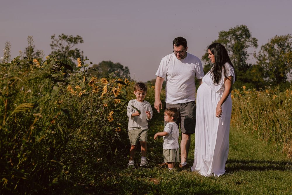 People in white outfits stand together in a meadow with wildflowers and greenery during golden hour.