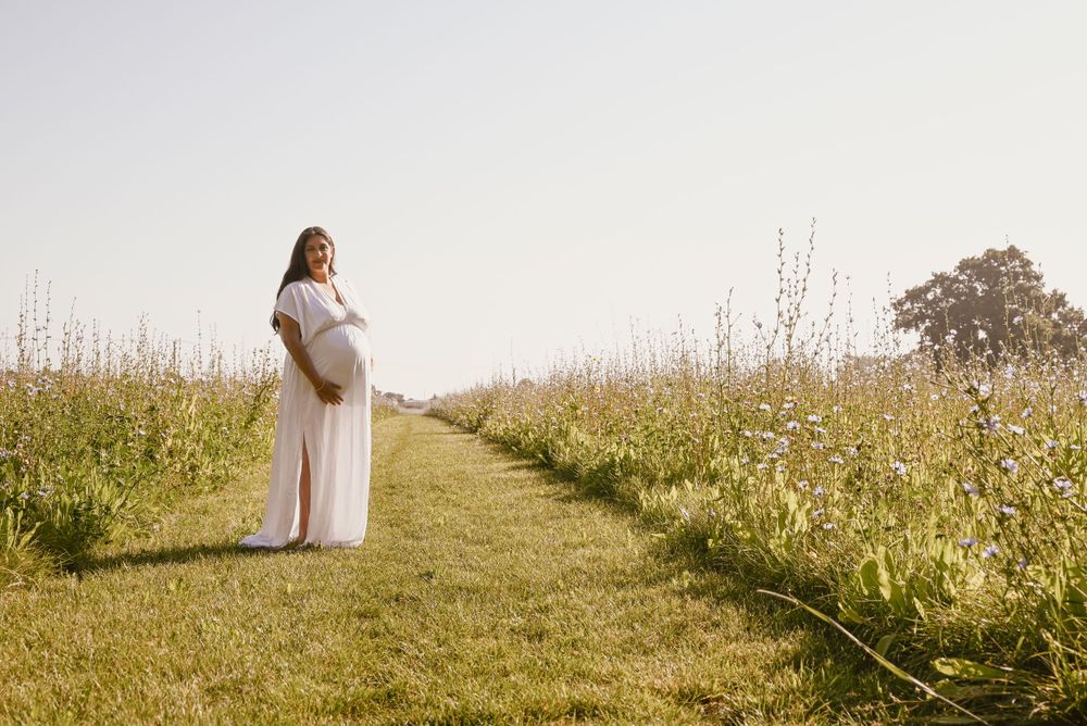 A person in white stands on a grass path through a wildflower meadow on a sunny summer day.