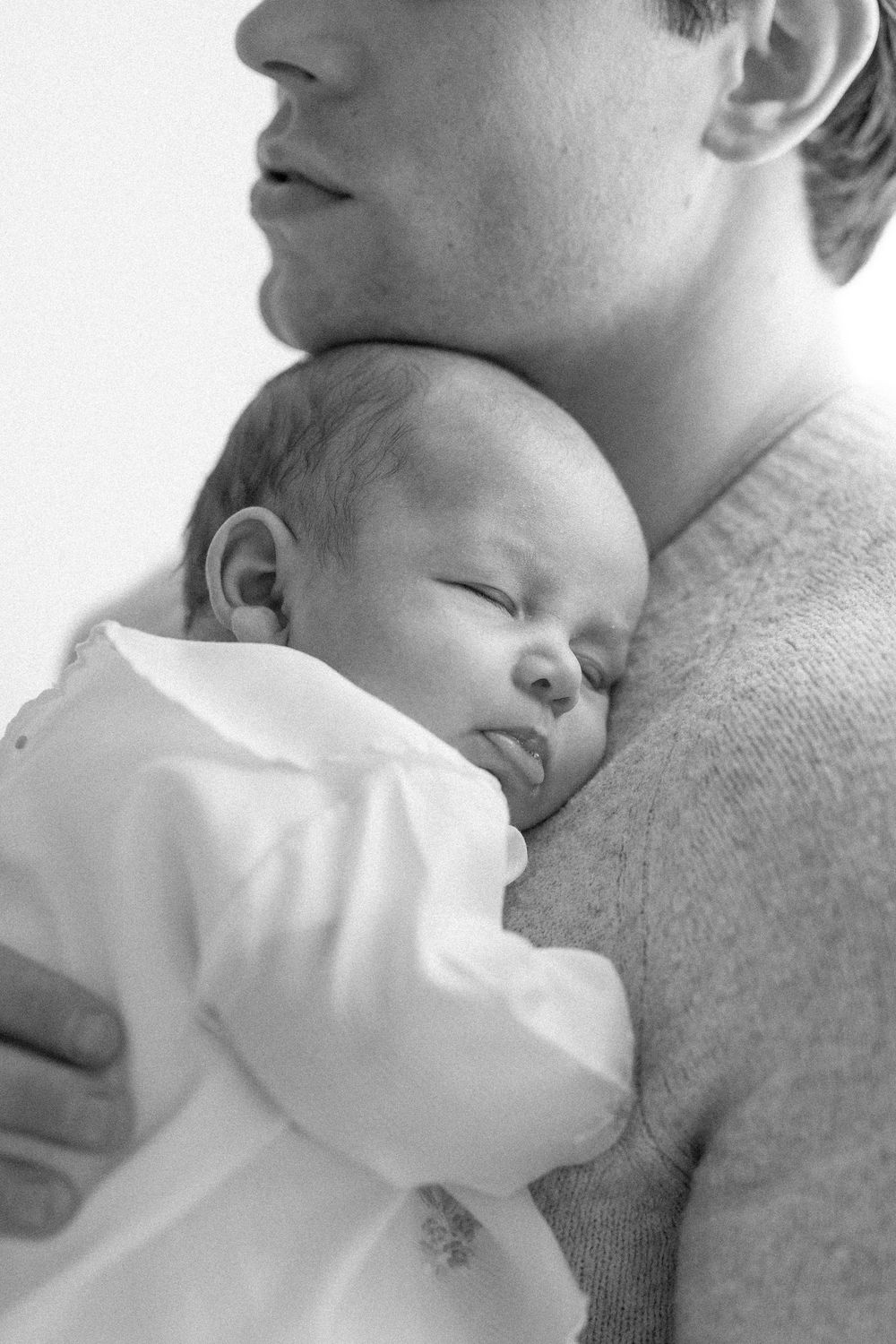 Black and white photo of a newborn baby sleeping peacefully on a parent's chest in a cozy sweater.