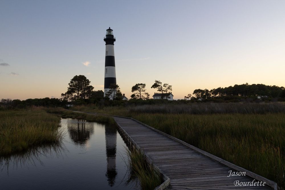 Bodie Island Lighthouse stands tall against a vibrant sunset sky, its black and white stripes contrasting with the cool hues of sunset