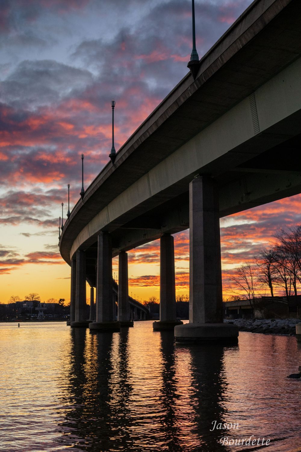 The underside of a highway overpass right at sunset with the sky like cotton candy. Color reflects in the calm water