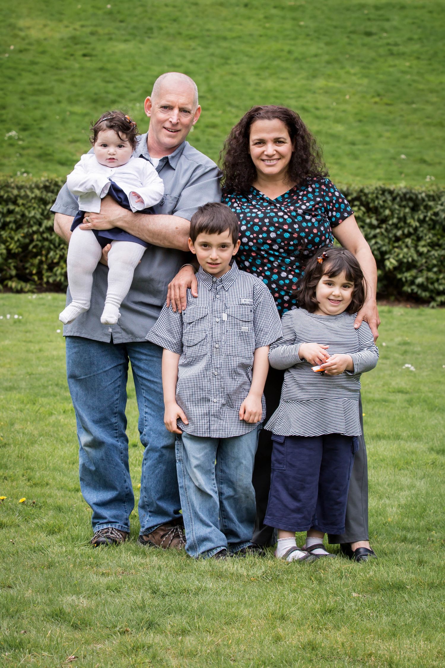 Family of five posing together on green lawn in casual attire.