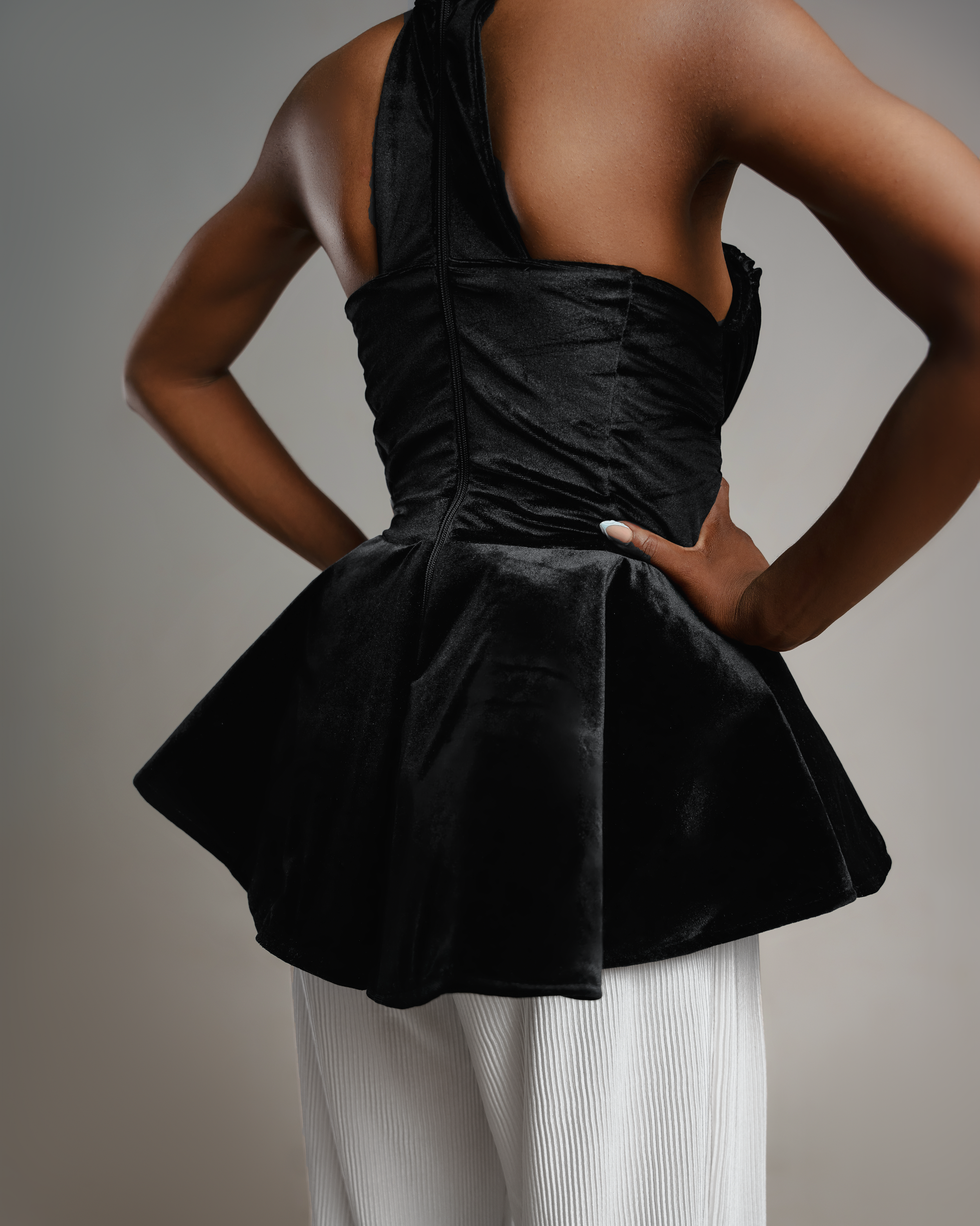 Black velvet peplum top with fitted waist shown against grey studio background.