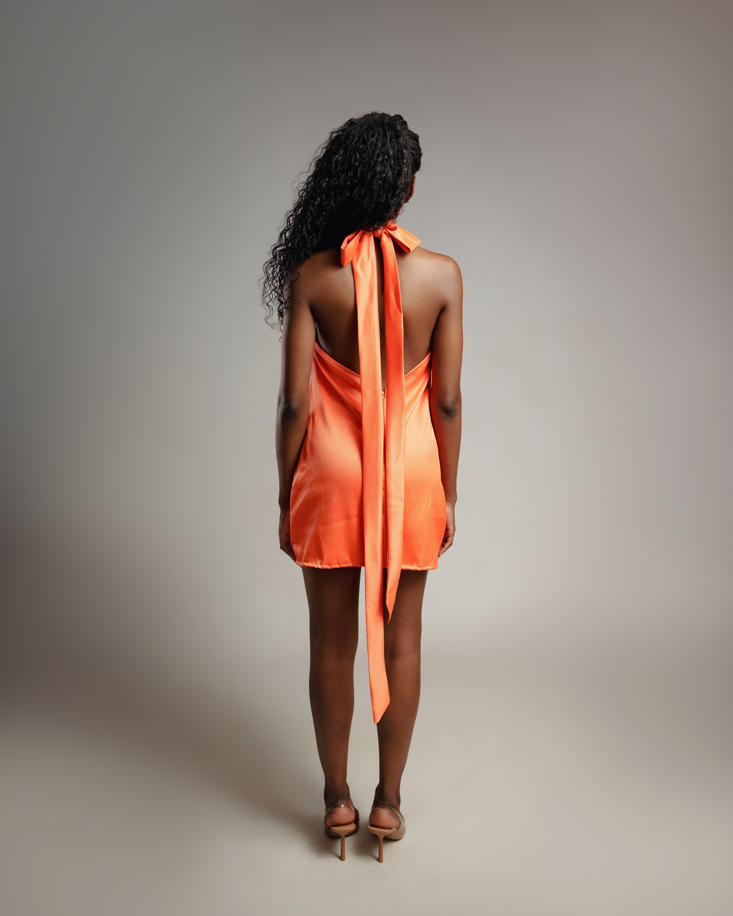 Back view of coral halter mini dress with flowing tie detail.