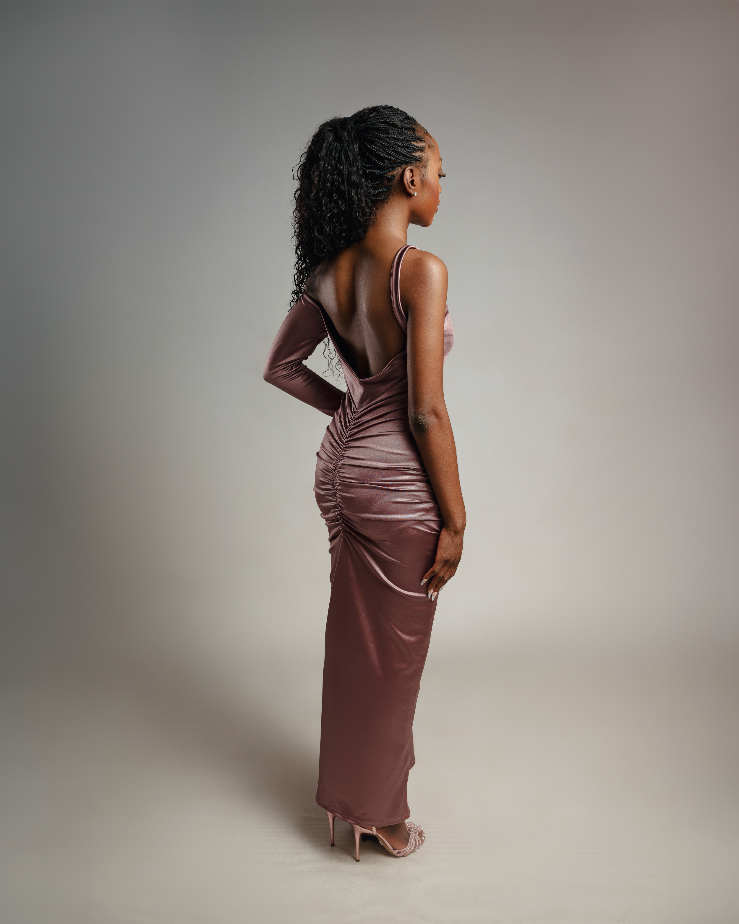Side view of model in fitted mauve satin evening gown against grey backdrop.