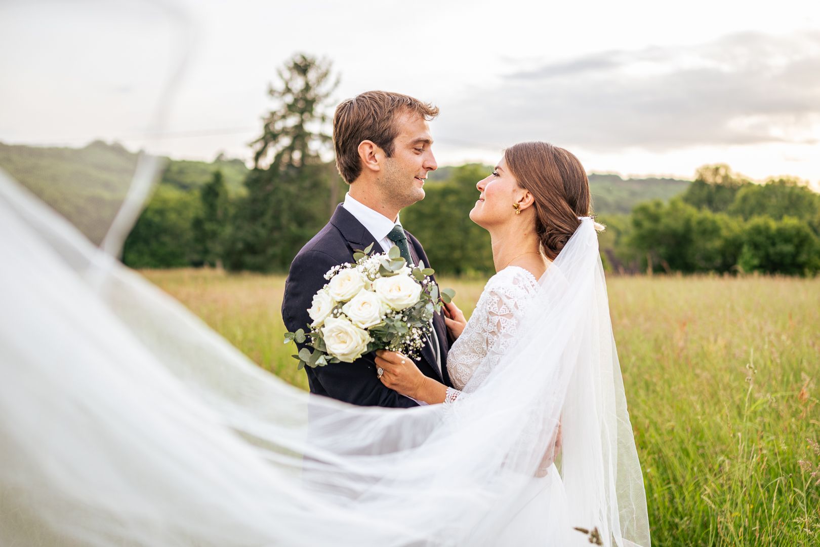 A romantic wedding portrait of a couple in a field with the bride's veil flowing in the wind.