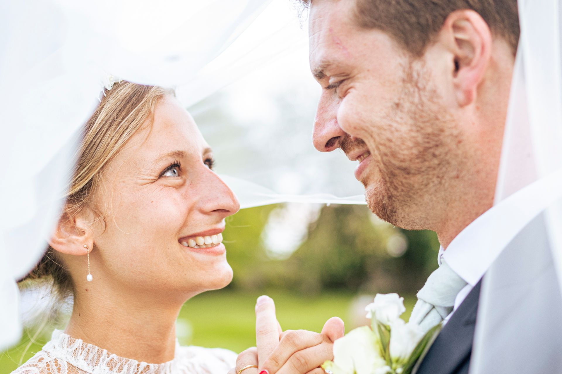 A joyful wedding couple sharing an intimate close-up moment outdoors.