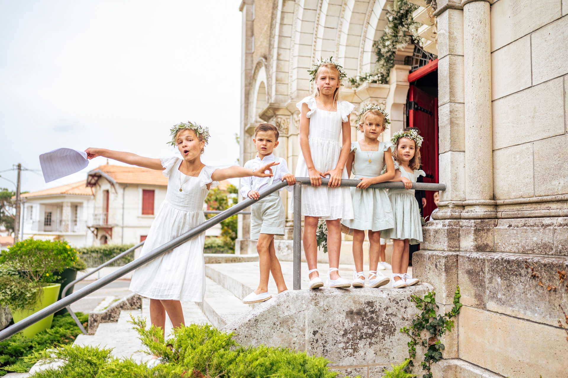 Young flower girls in white dresses posing on church steps with floral decorations.