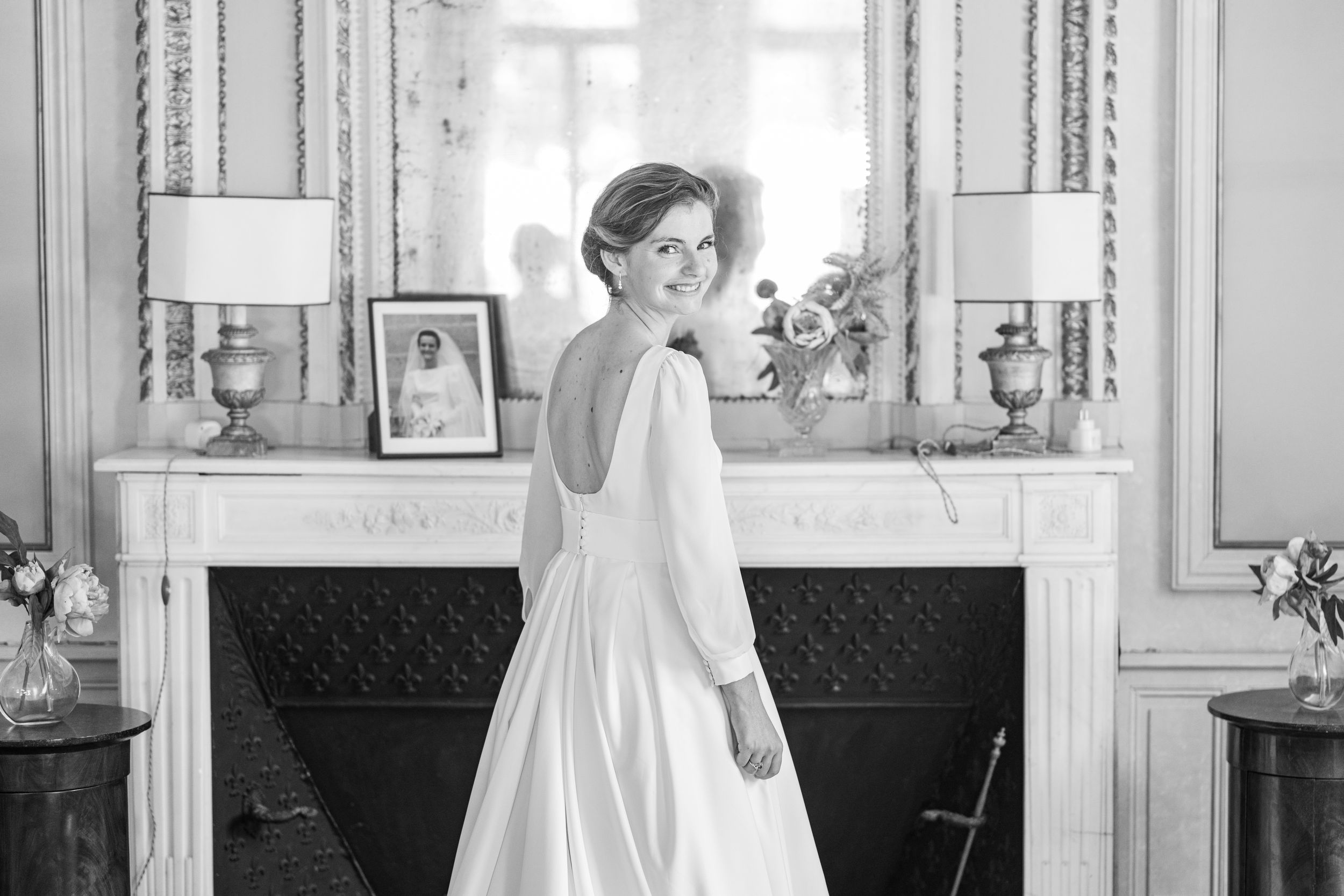 A elegant bride in a classic white gown poses by a fireplace in black and white.