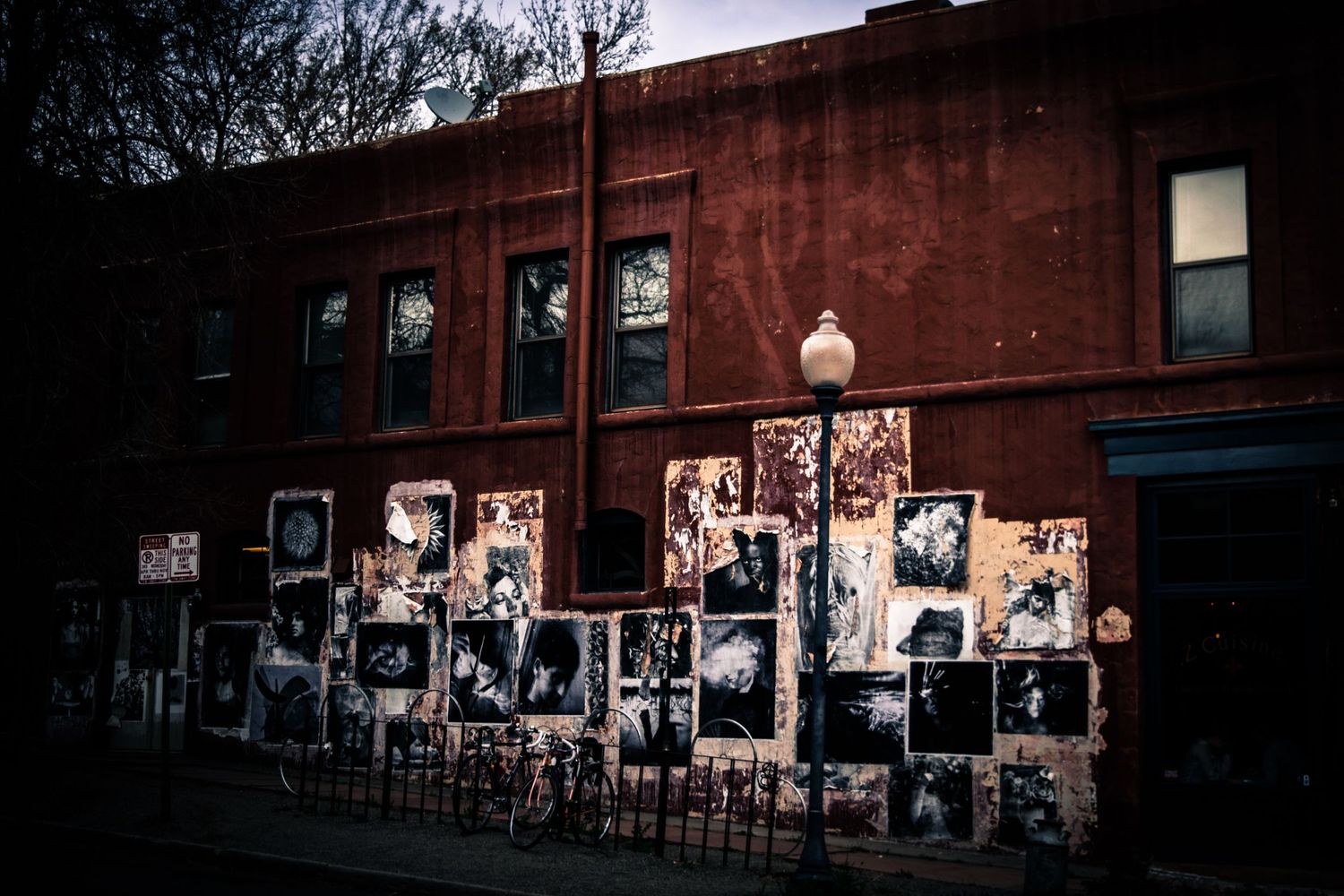 Red brick building wall covered with weathered posters and photographs.