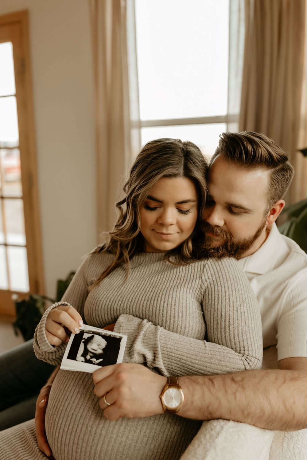Intimate couple's maternity photography session in warm natural light with beige sweaters.