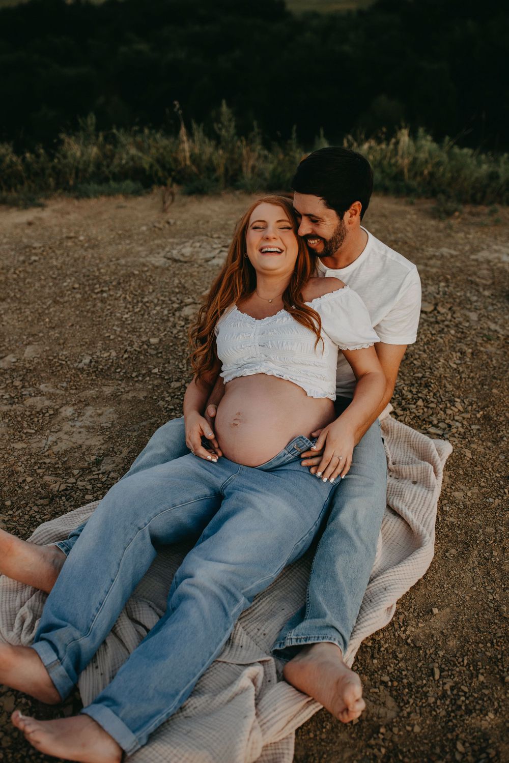 Intimate maternity photo of couple relaxing on blanket outdoors at sunset.