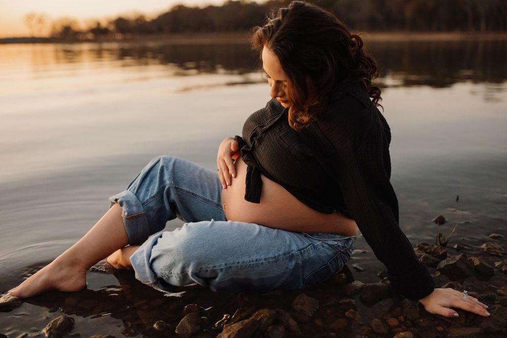Two people in casual attire sit close together on a beach at sunset creating a romantic silhouette against the water.