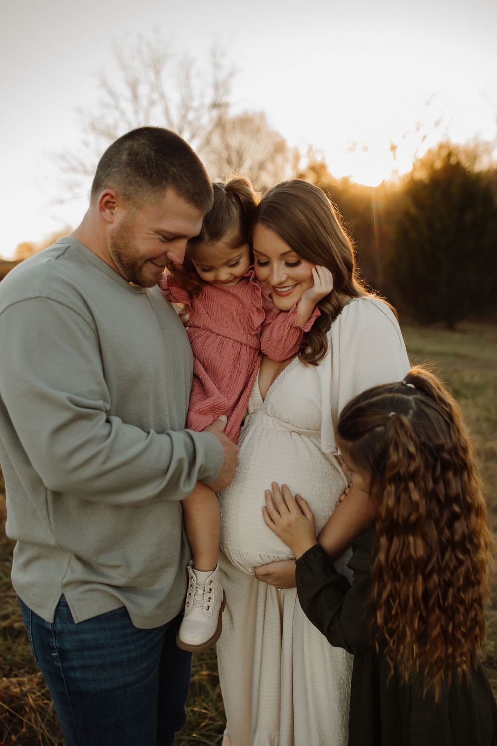 A family shares tender moments together in a golden-lit outdoor setting during sunset.