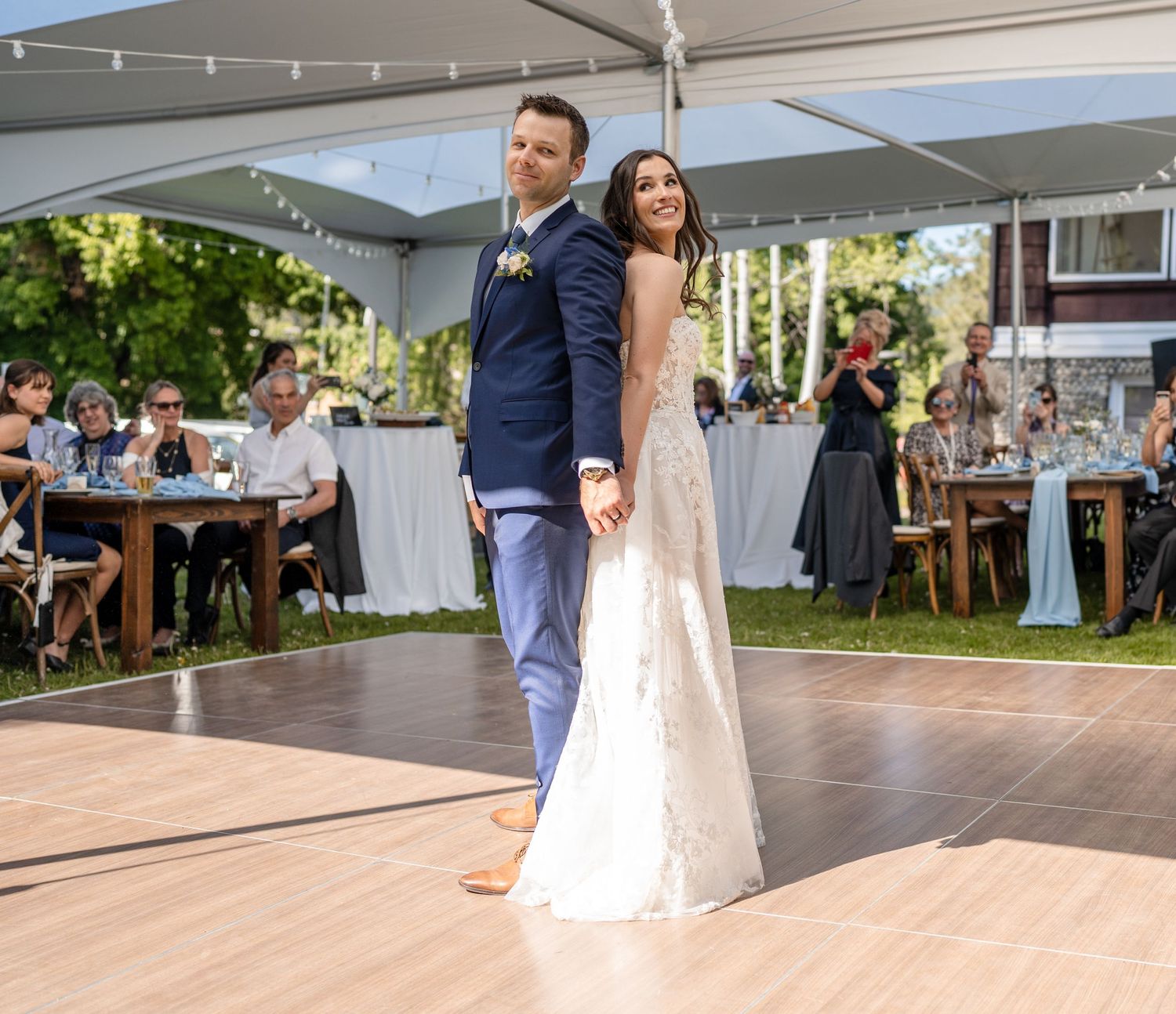 A couple dances at an outdoor wedding reception under a white canopy with tables of guests in the background.
