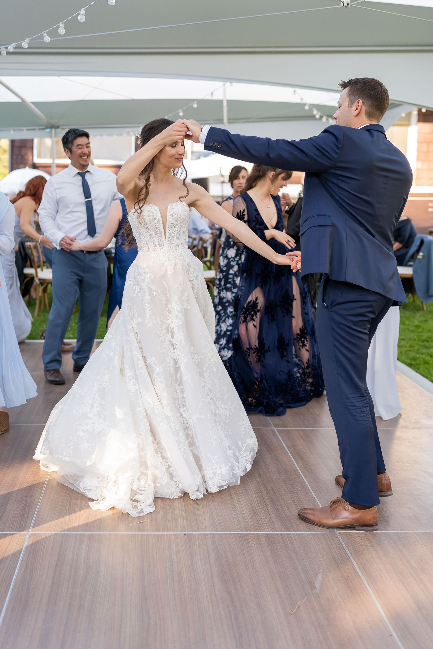 A couple shares their first dance on a wooden dance floor under an outdoor tent.