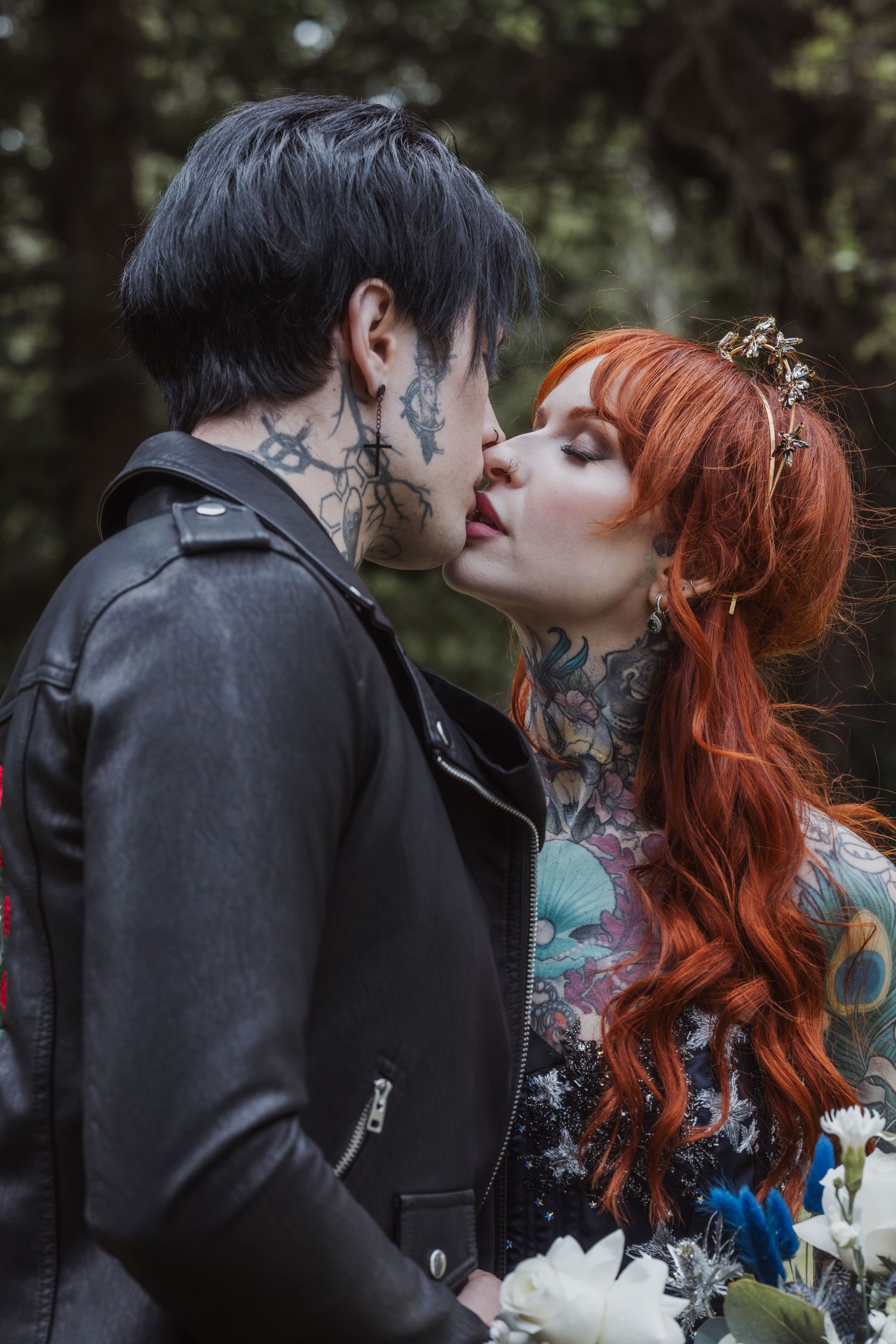 Tattooed couple sharing a kiss, with the groom in a black leather jacket and the bride with red hair, holding a bouquet.