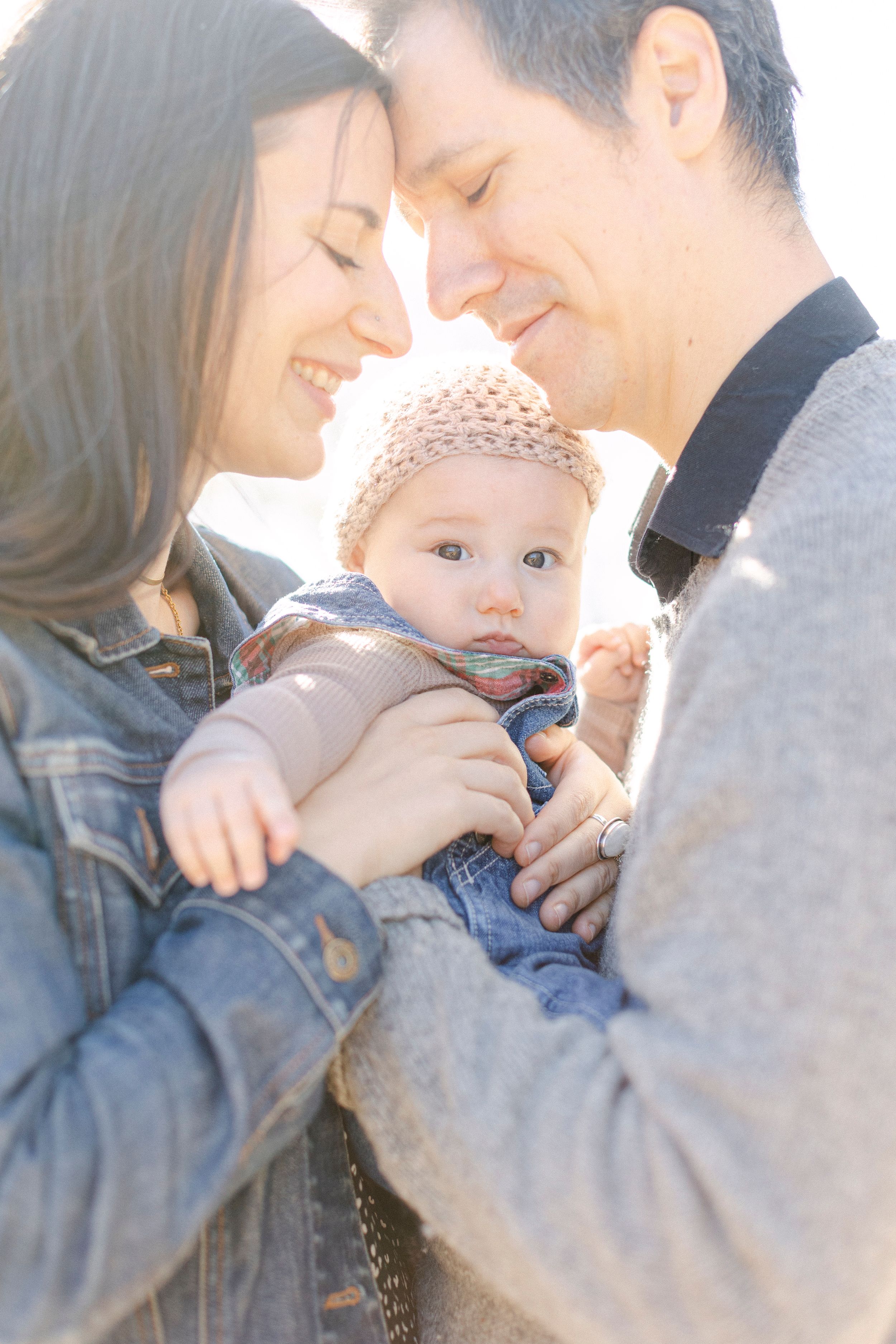 Intimate family moment outdoors with baby in knit hat and denim outfit.