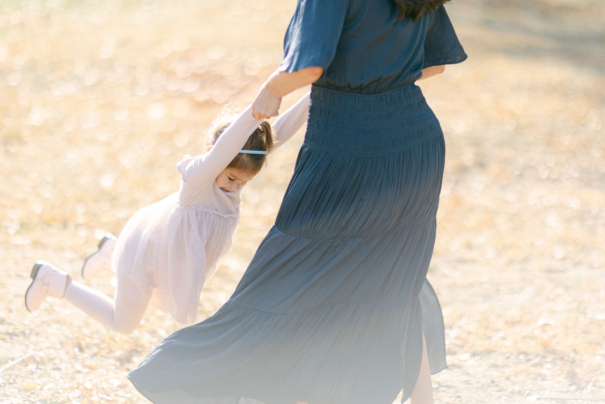 A playful spinning dance moment between two figures in a sunlit field.