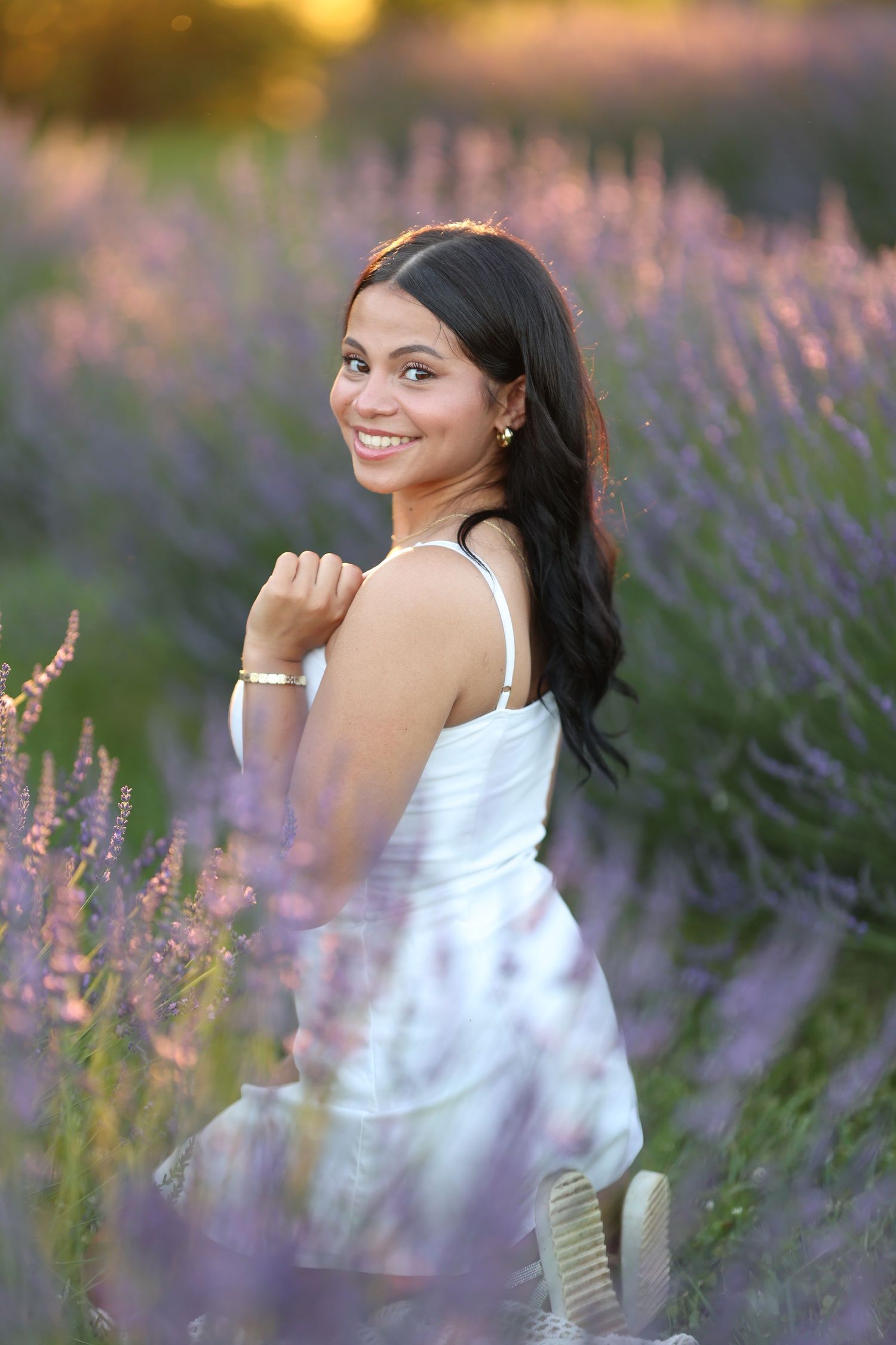 A senior girl in a white dress poses joyfully among blooming purple lavender flowers at sunset.  Middle Tennessee Best Senior Photographer