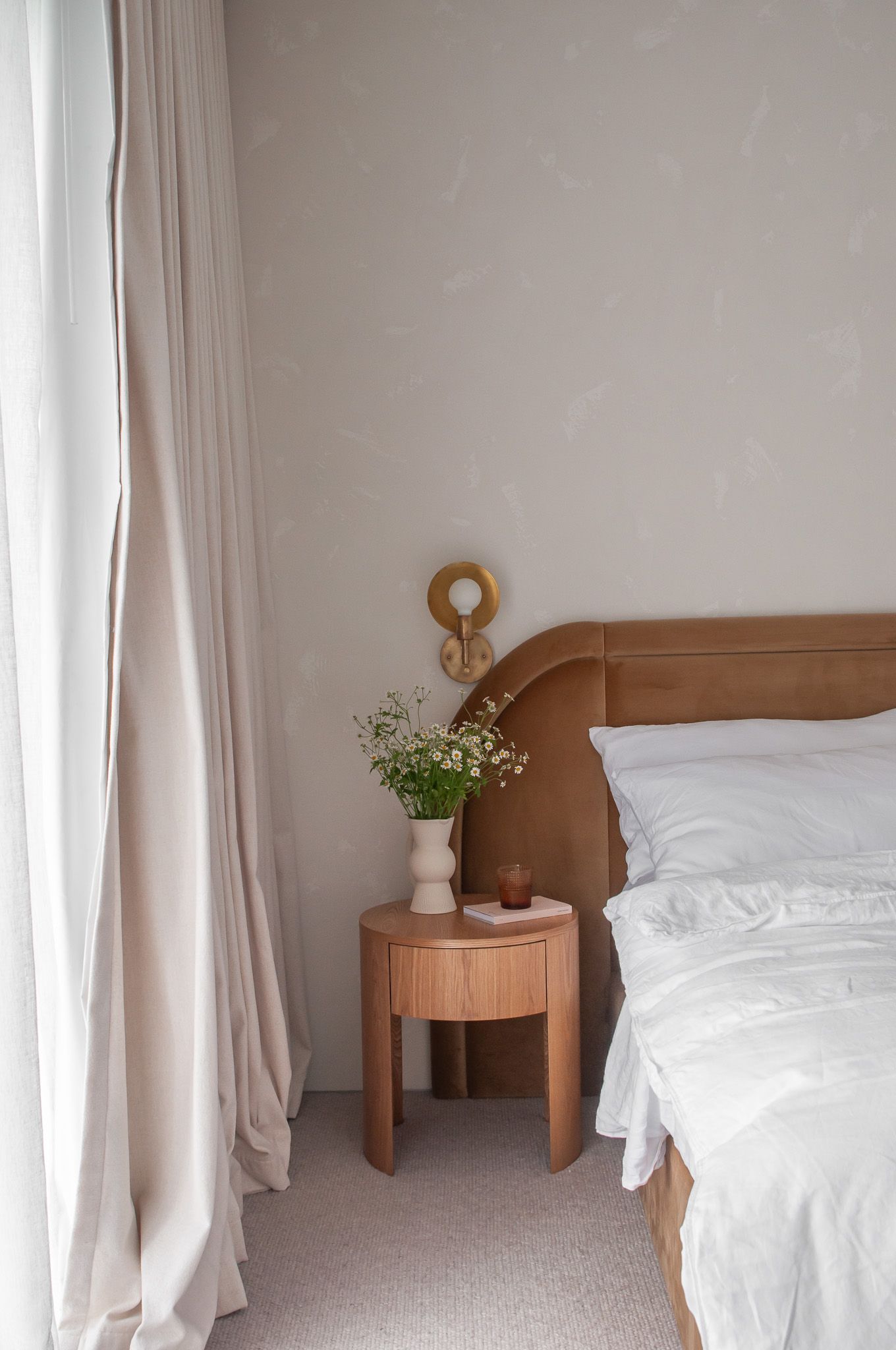 Serene bedroom corner with wooden side table, white bedding, and natural light from window.