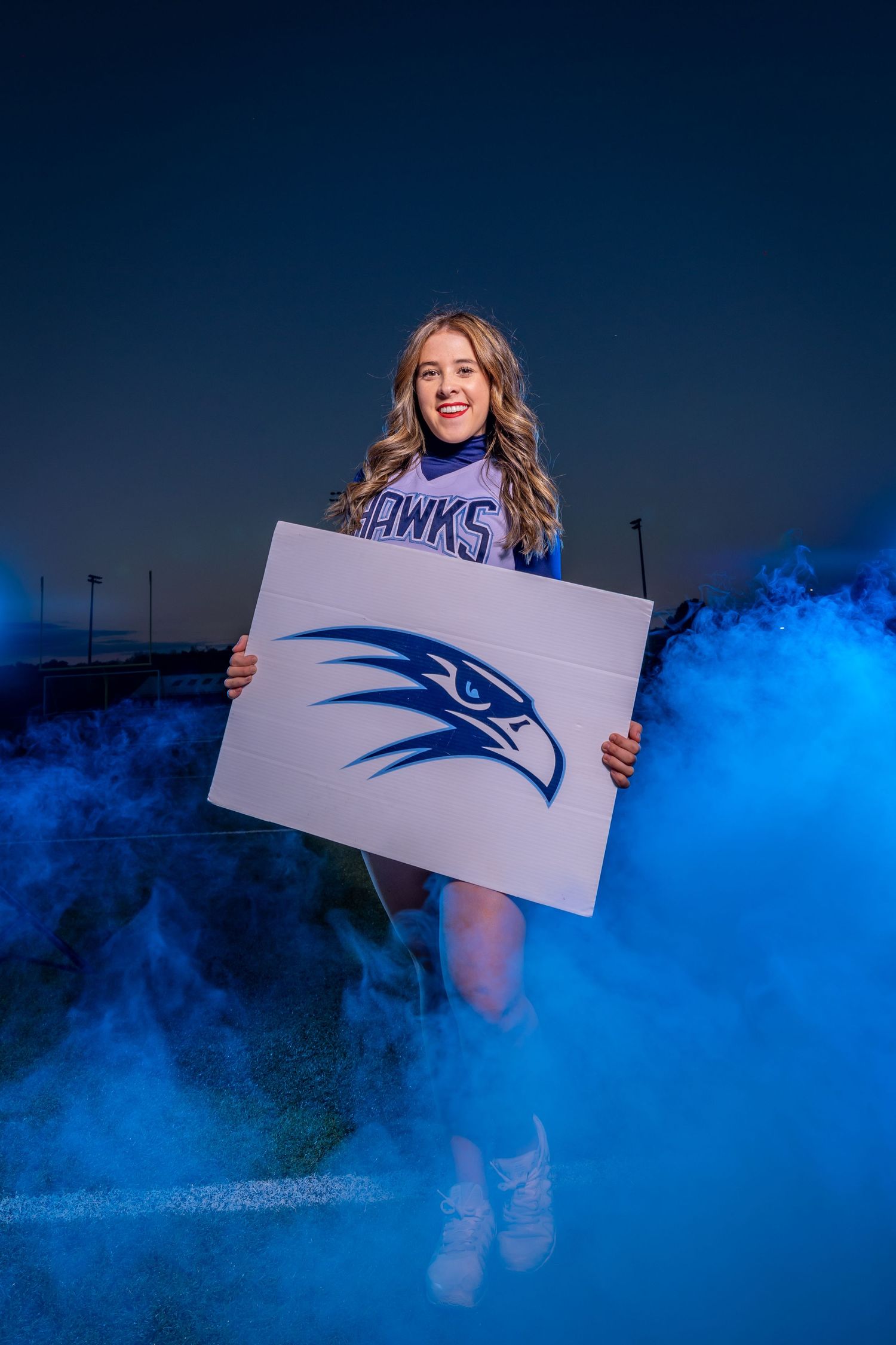 A Seattle Seahawks fan holds up team logo sign surrounded by blue smoke effects during evening photoshoot.