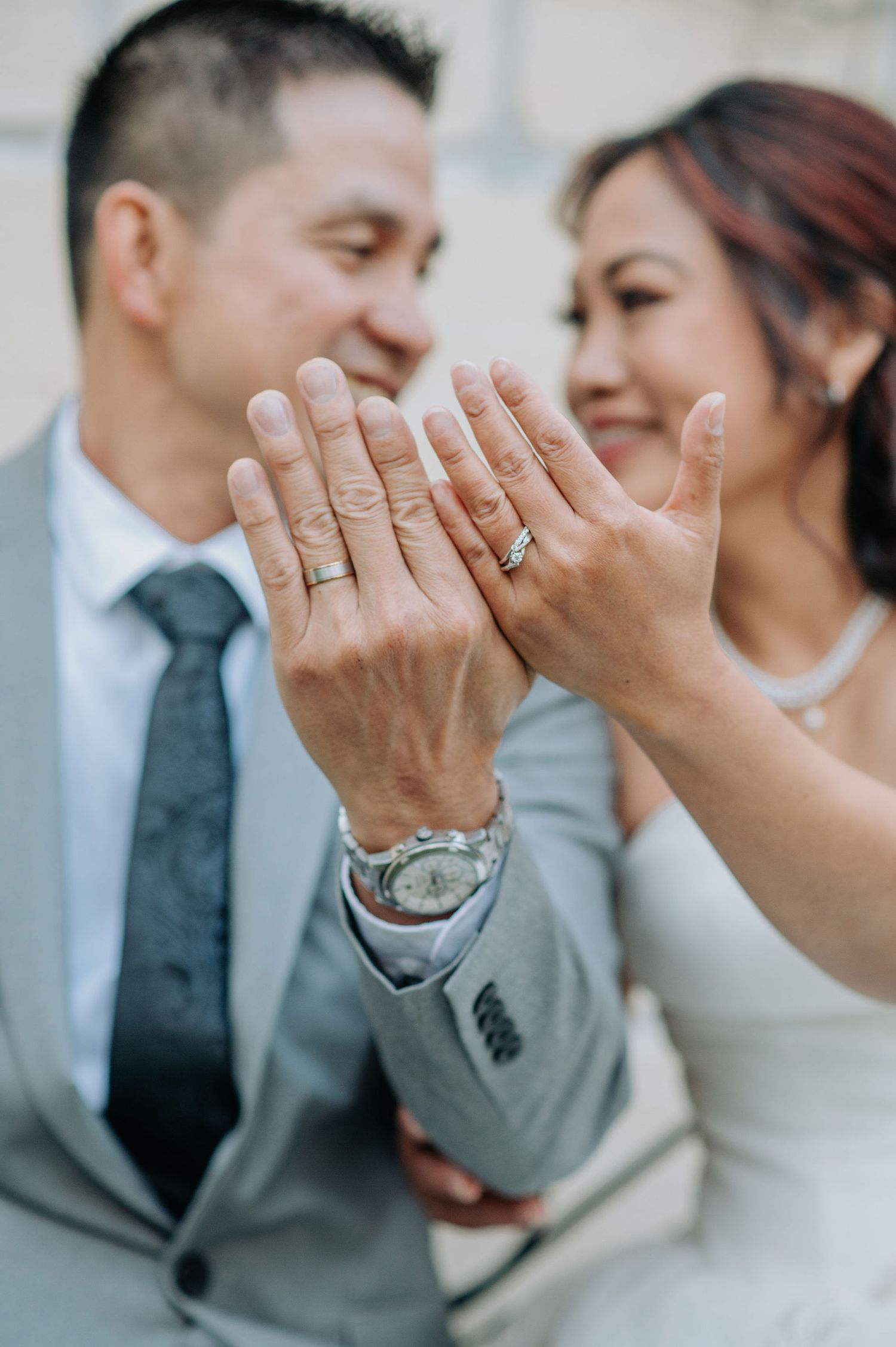 Close-up of newlyweds showing off their wedding rings with joyful expressions.