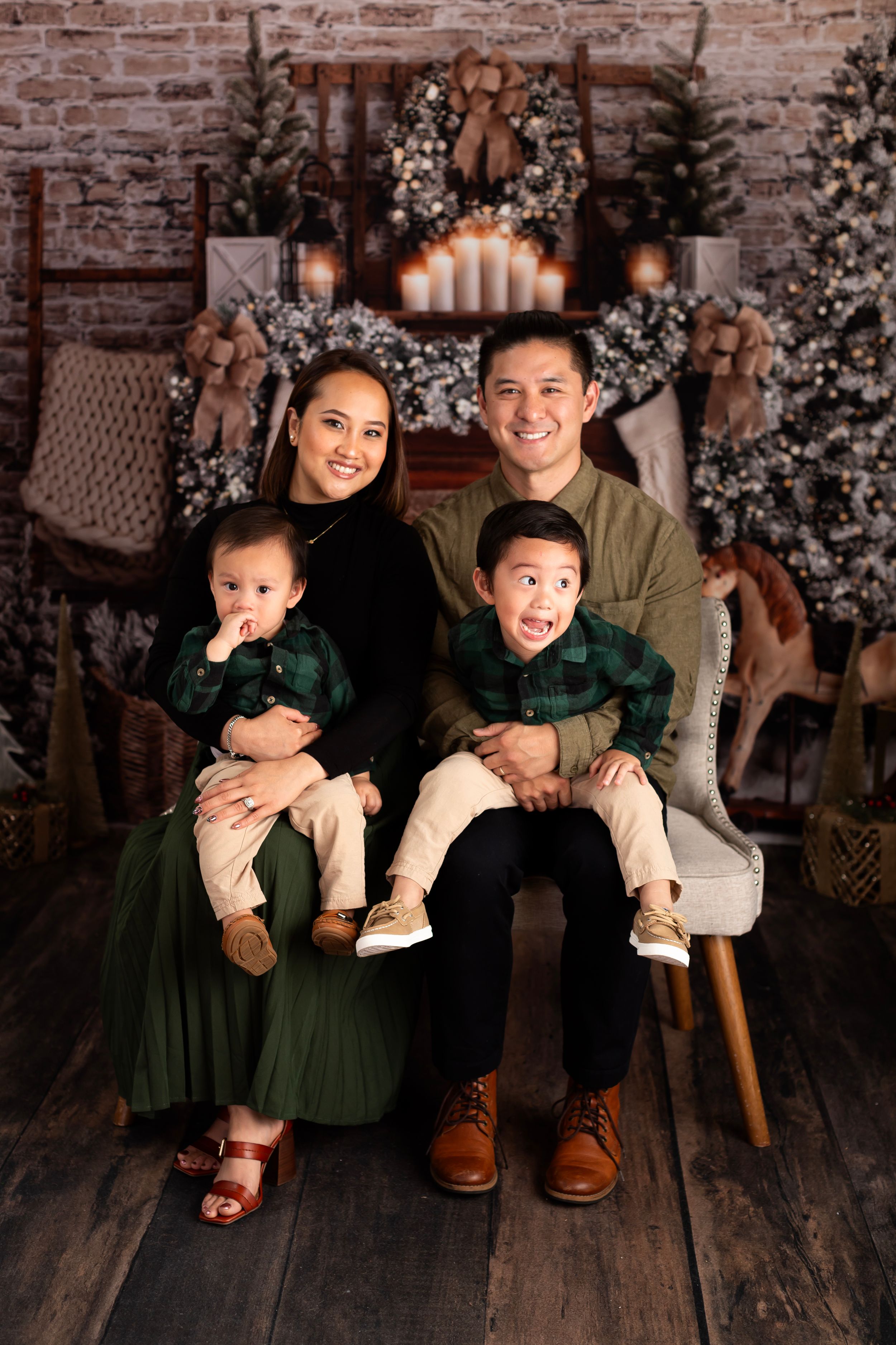 Family Christmas portrait with matching green outfits against a decorated brick wall backdrop.