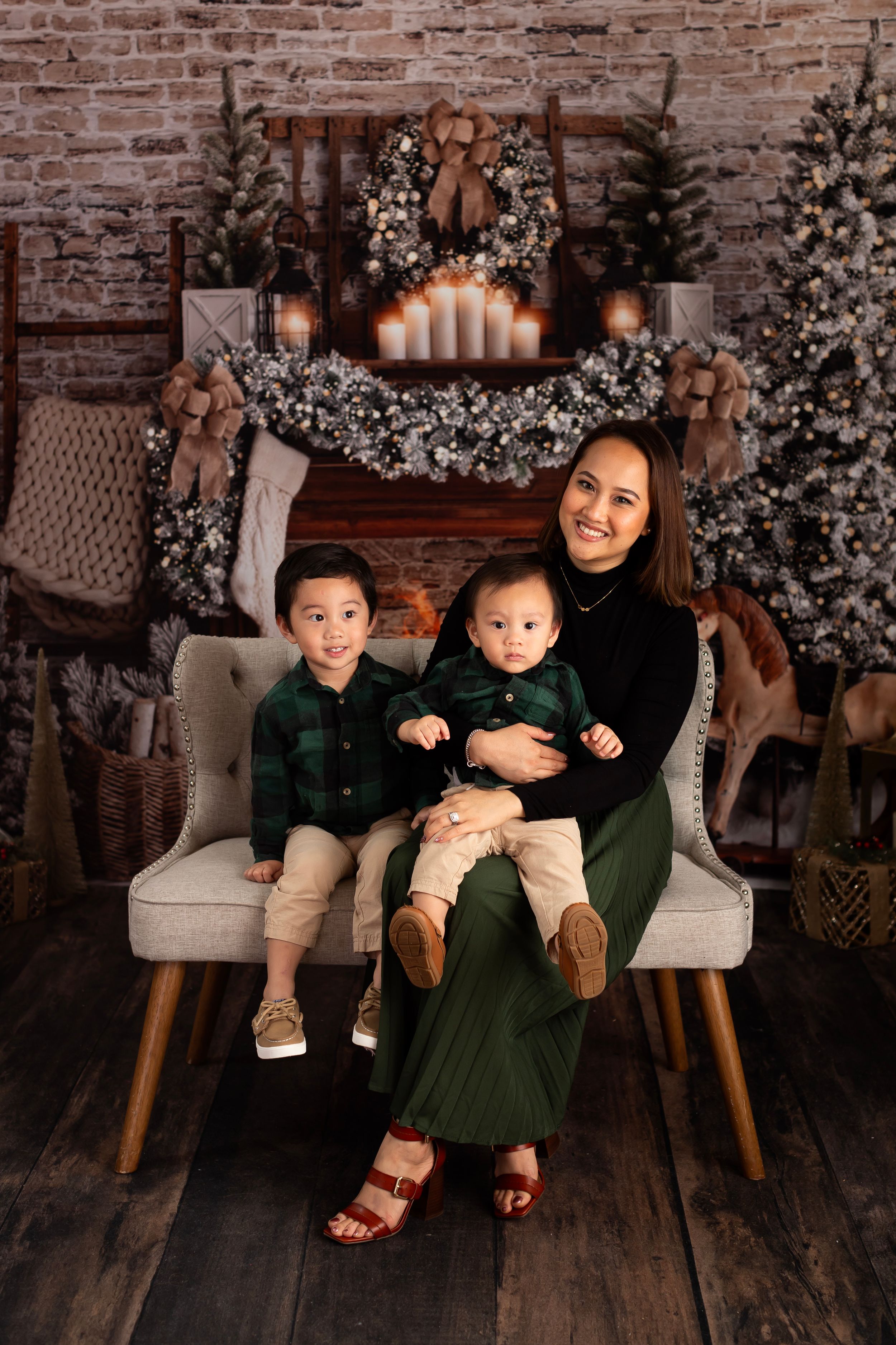 A cozy holiday portrait in front of a rustic fireplace with Christmas trees and festive decorations.