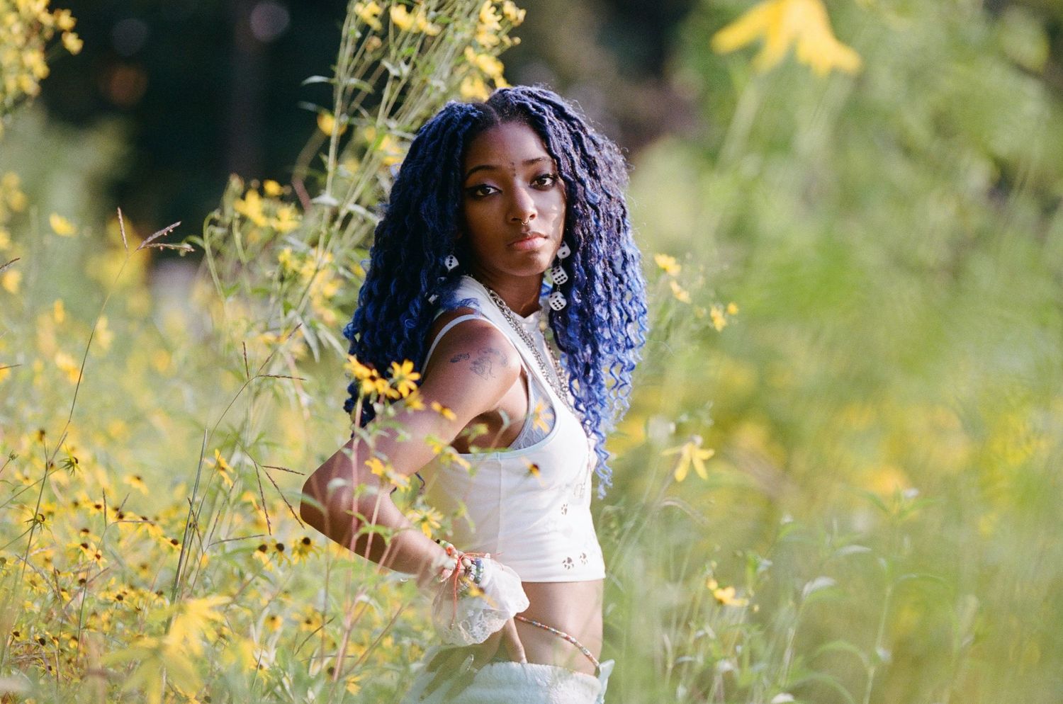 A figure in white clothing sits among blooming yellow wildflowers in a natural setting.