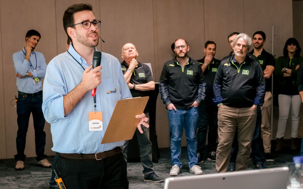 Corporate speaker with microphone and clipboard addresses a group during a team building event.