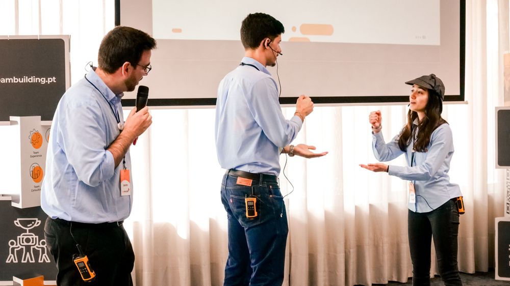 Two facilitators with microphones interact with a participant during a team building workshop presentation.