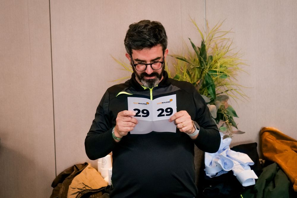 Man with glasses reads a document showing number 29 during a corporate team building event.