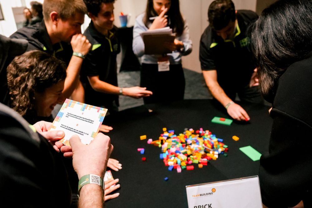Team members collaborate around a table with colorful building blocks during a team building challenge.