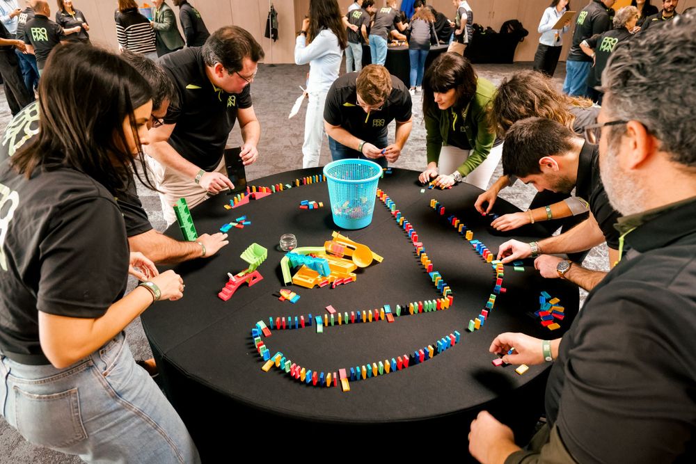 Corporate team arranges colorful dominoes in an intricate pattern on a round black table during team building.