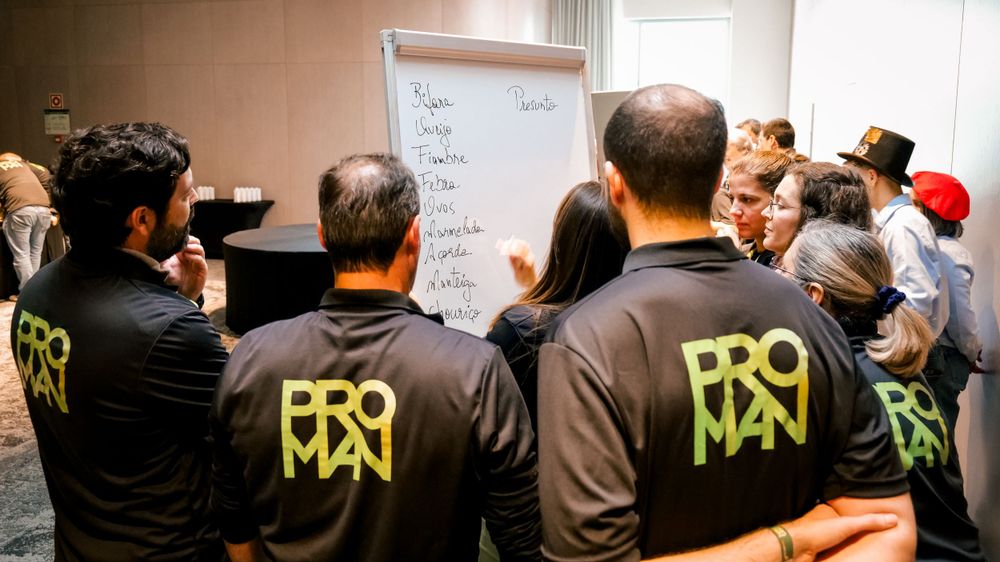 Group of professionals in PROMAN black shirts collaborate around a whiteboard during a corporate training session.