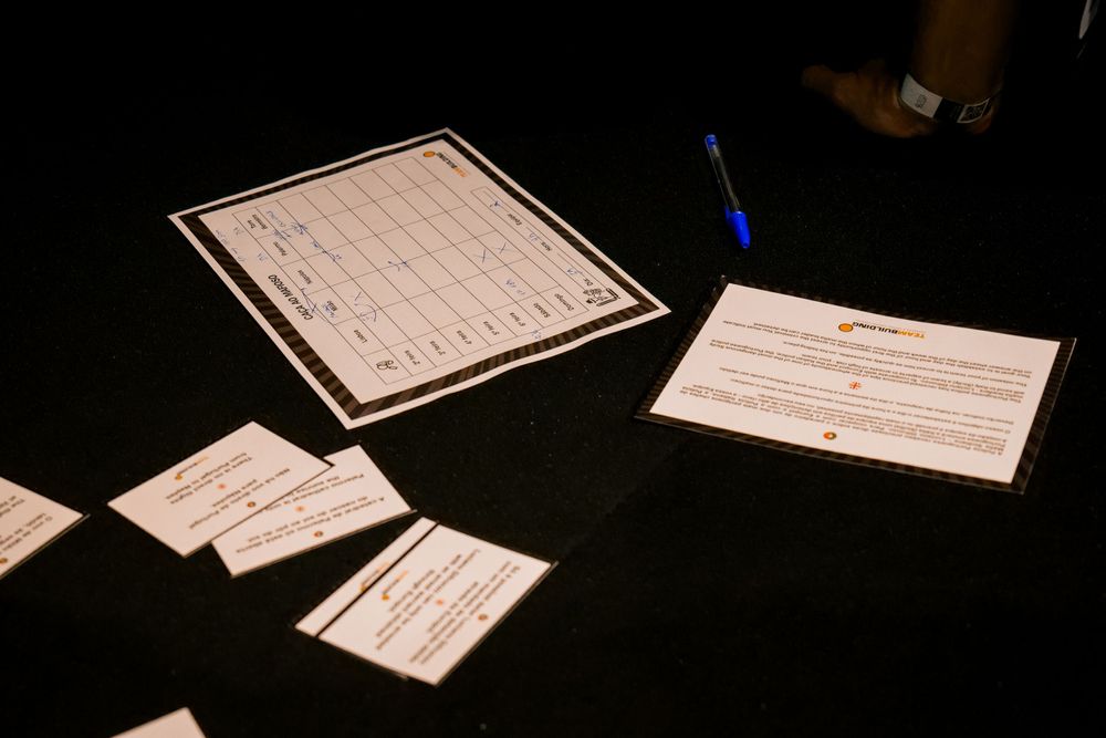 Corporate workshop materials including printed sheets and cards spread on a dark table with a blue pen.