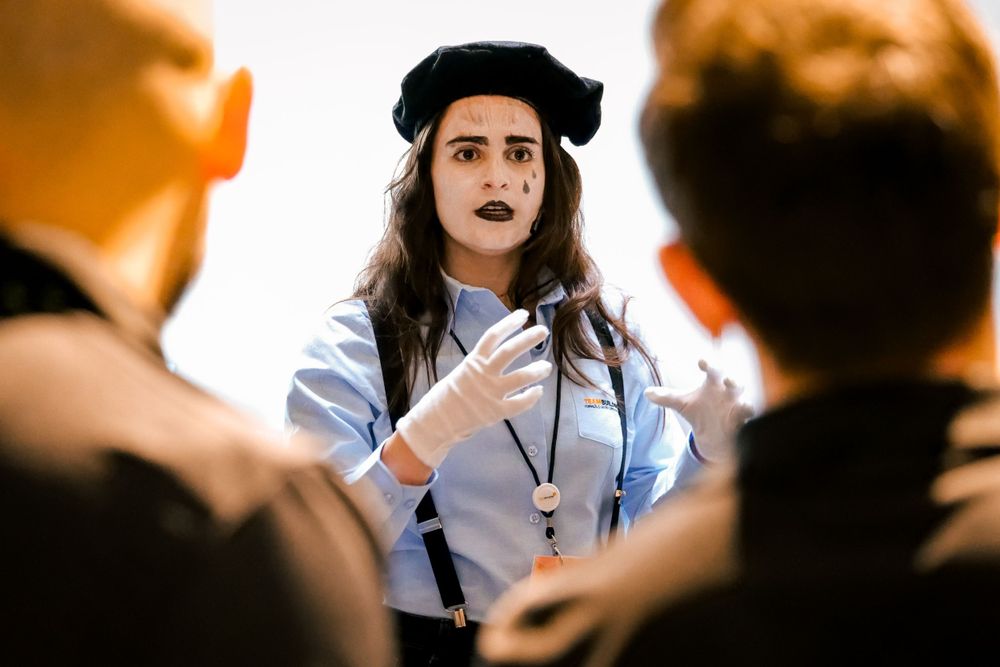 A mime performer in white face paint and beret engages with participants during a corporate event.
