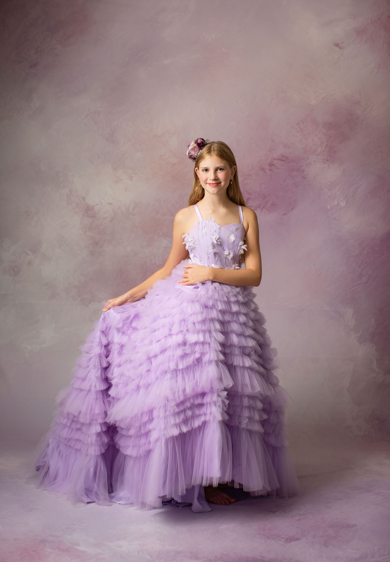 Elegant lavender ball gown with tiered tulle ruffles photographed against a soft purple background.