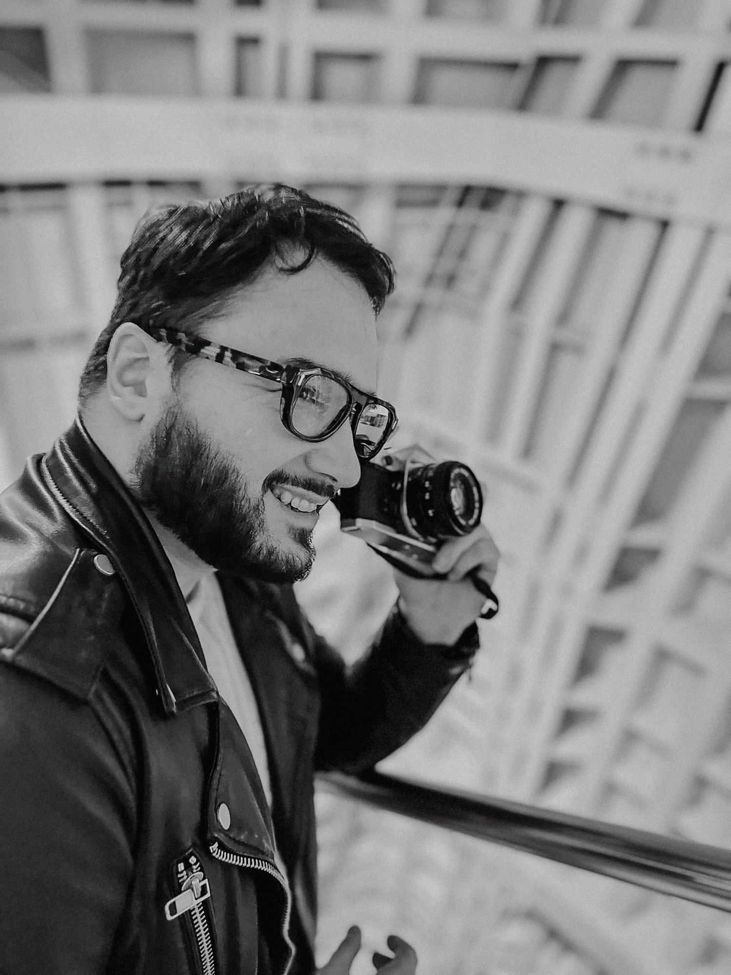 Professional male photographer holding a camera, wearing glasses and a navy blazer, posing against a dark background.