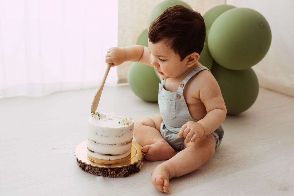 Baby crawling near birthday cake with green balloon decorations.