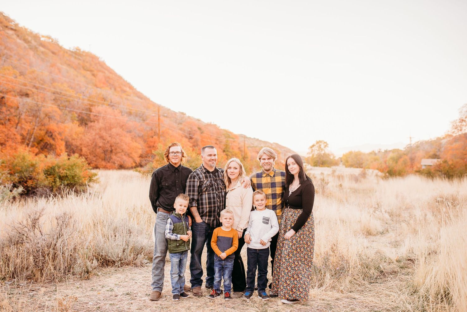 A family poses together in front of autumn foliage and mountains on a golden-hour evening.