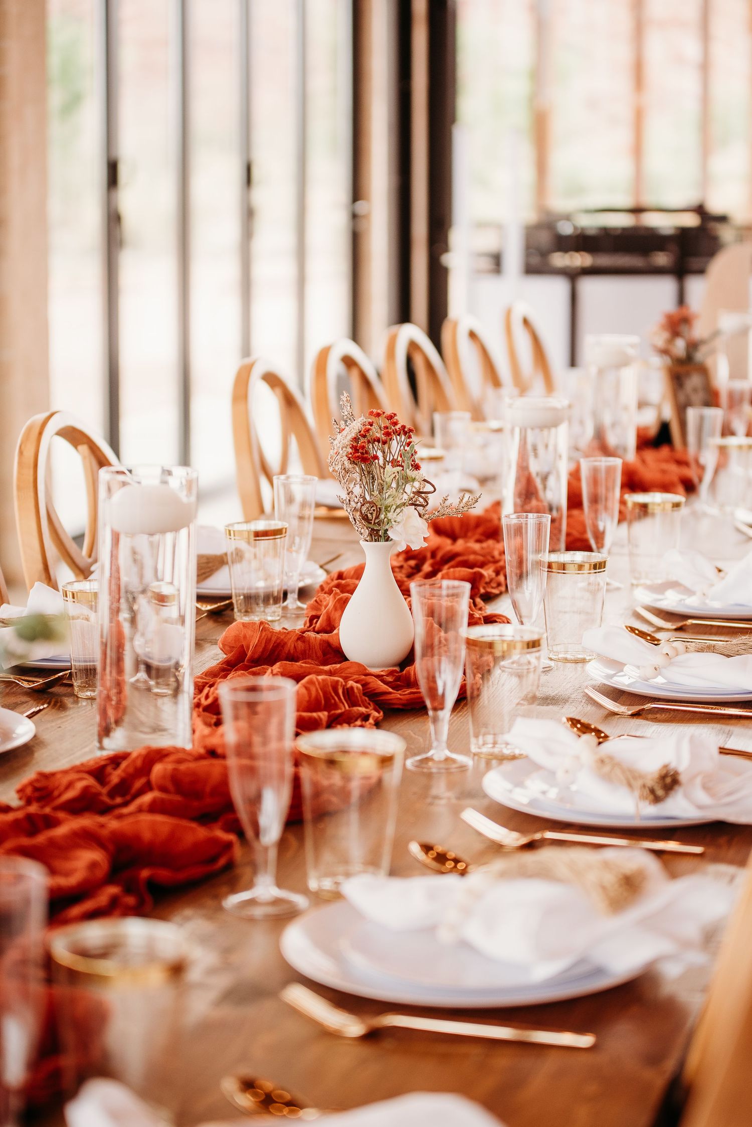 Elegant wedding table setting with coral runner, gold chairs, and white floral centerpieces.