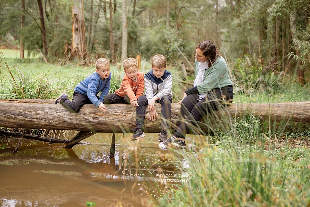Group engaged in outdoor nature exploration while sitting on fallen log by muddy pond surrounded by green foliage.