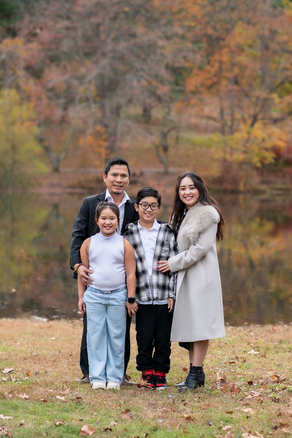 Family of four poses by a colorful autumn lake in a warm outdoor portrait.Holmdel Park NJ
