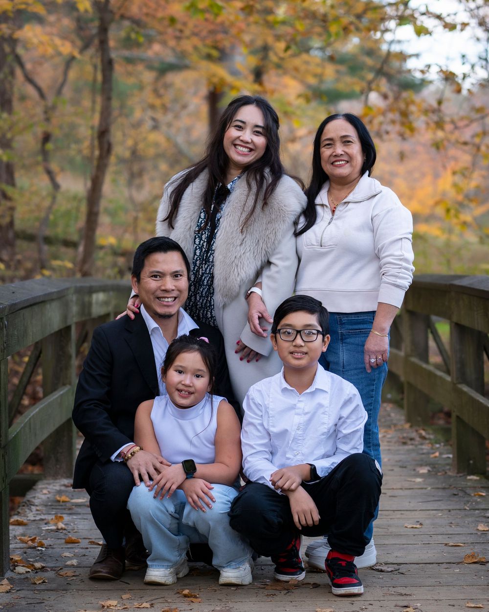 Family of five poses on a wooden bridge surrounded by beautiful fall foliage colors.Holmdel Park NJ