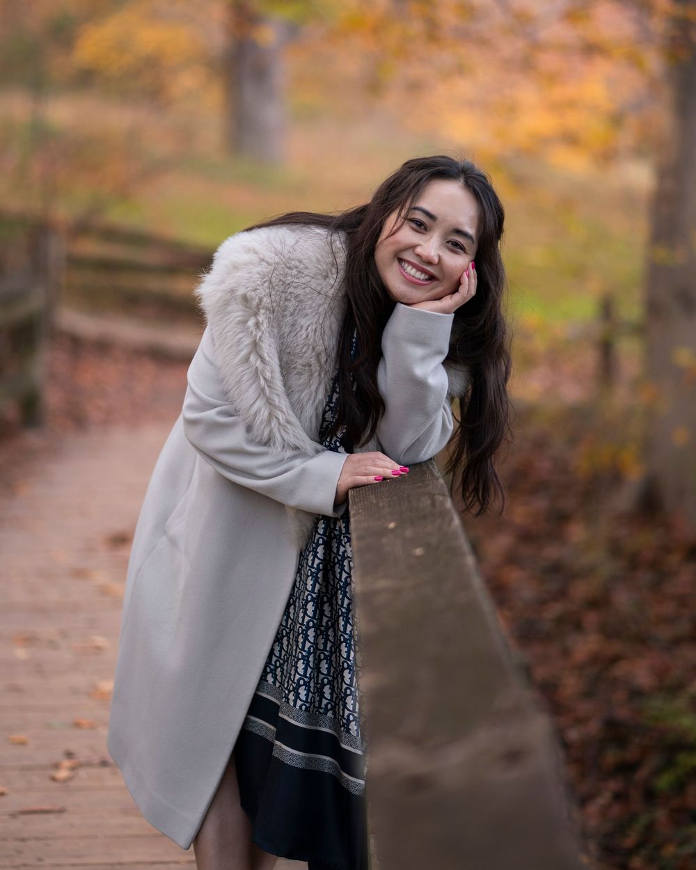 Young woman leans on a wooden bridge railing smiling in a colorful autumn park.Holmdel Park NJ